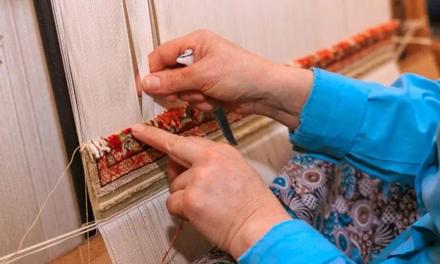 a women placing knots in a carpet, knot density is higher in carpet.
